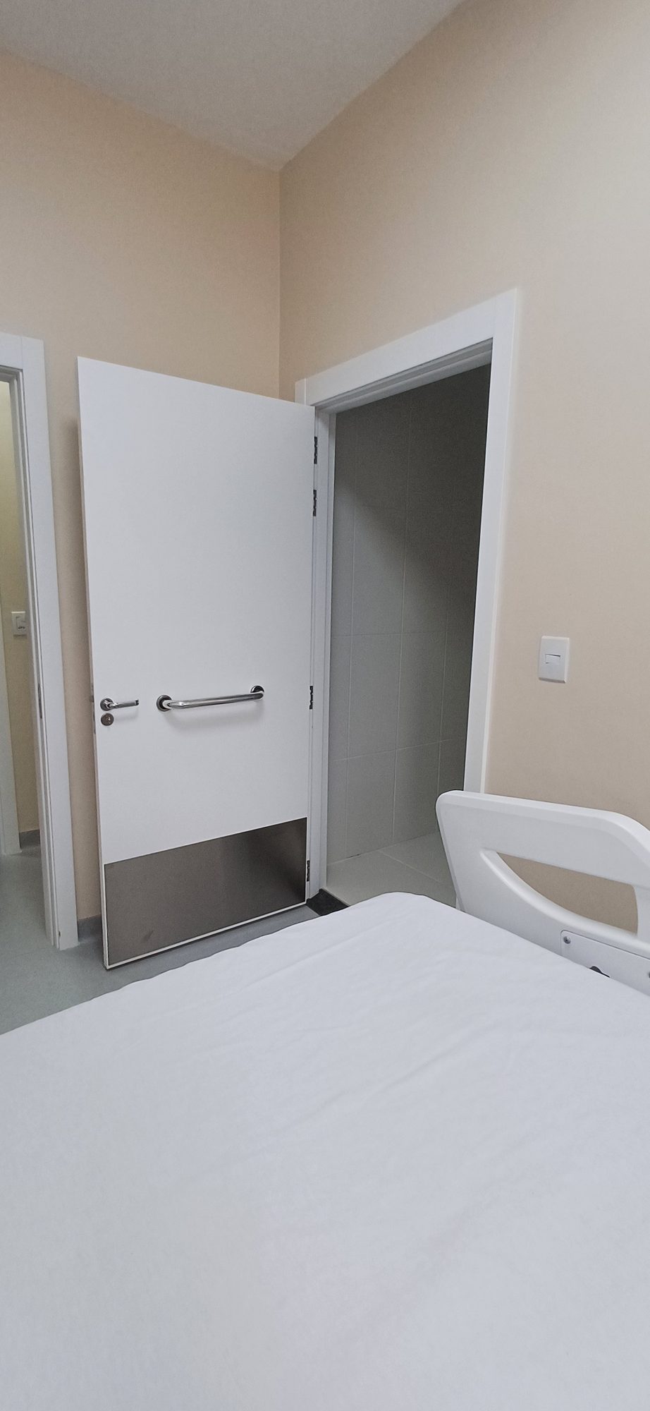 Porta de quarto hospitalar aberta, com barra de apoio e chapa inox na base.