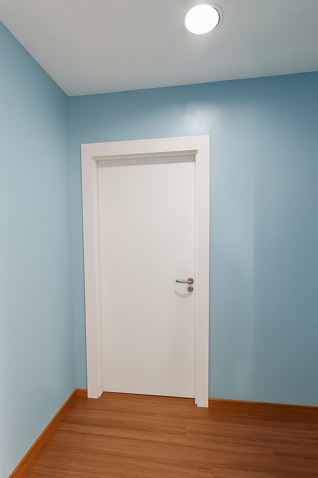 Porta de giro lisa branca em quarto hospitalar com parede azul.